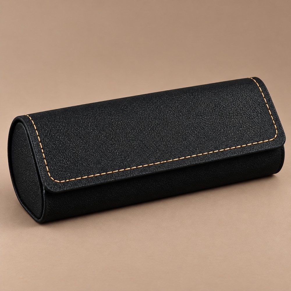 Black textured flap-top glasses case with tan contrast stitching and a rounded body on a taupe background.