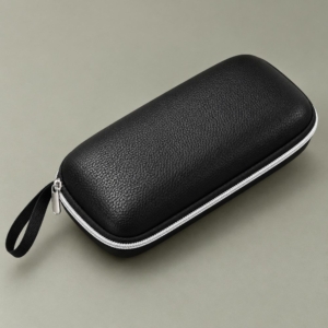 Black rectangular zipper glasses case with a pebbled finish, contrasting light-colored zipper and black carry loop on a sage-grey background.
