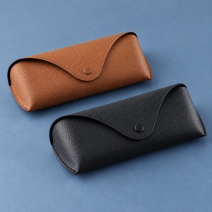 Brown YX12 PVC faux leather glasses case with a pebbled surface, curved flap and matching press stud on a greige background.