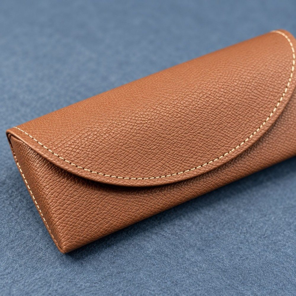 Close-up of lychee-grain PVC faux leather and cream stitching on a brown glasses case