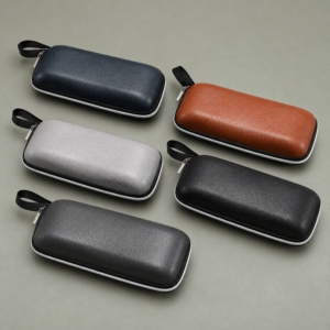 Matching zipper glasses cases in navy, brown, light grey, black and dark grey, each with a contrasting zipper and black carry loop.