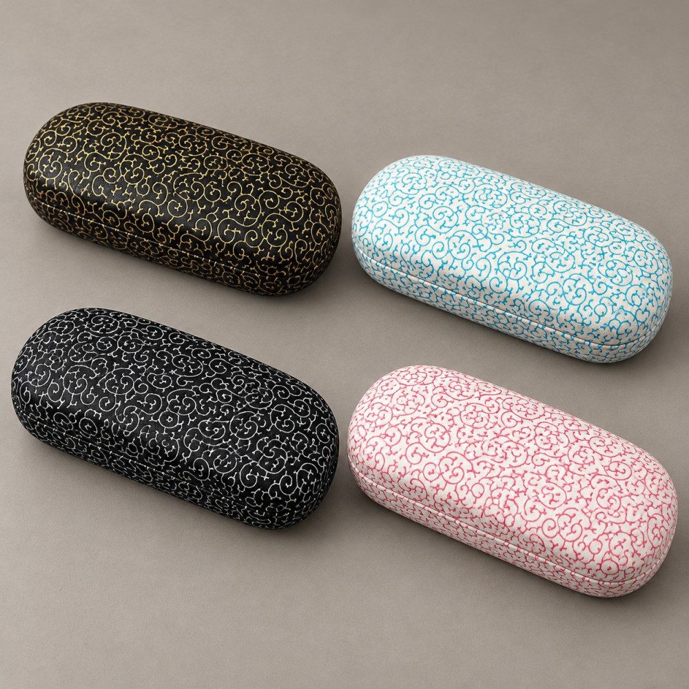 Four patterned metal eyeglass cases in black and gold, black and white, ivory and blue, and ivory and pink.