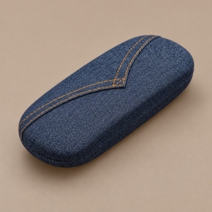 Indigo denim-look metal hard glasses case with a V-shaped panel and ochre double stitching on a taupe background.