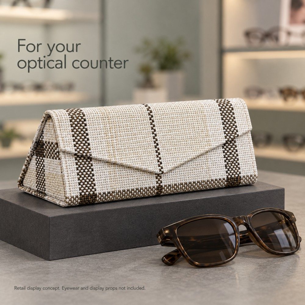 Ivory plaid foldable sunglasses case on a charcoal riser beside brown sunglasses in an optical counter display concept.