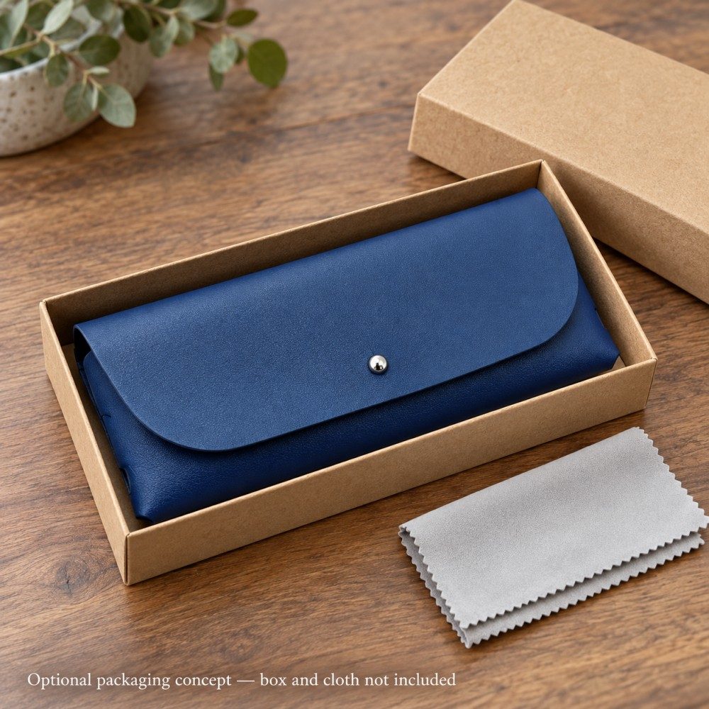Navy blue soft eyeglass case with a rounded flap, silver-tone front detail and slotted sides on a warm greige surface.