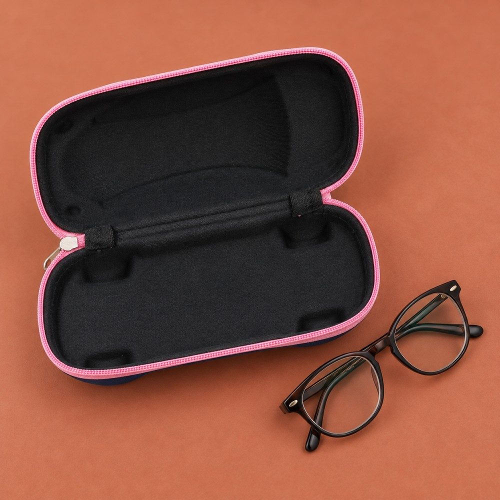 Hand placing a navy car-shaped glasses case with an orange-red zipper into a canvas tote