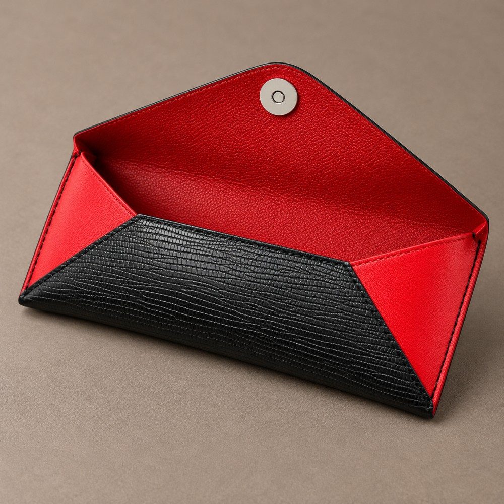Open black envelope glasses case showing its red interior, folded side panels and circular silver-tone closure component.