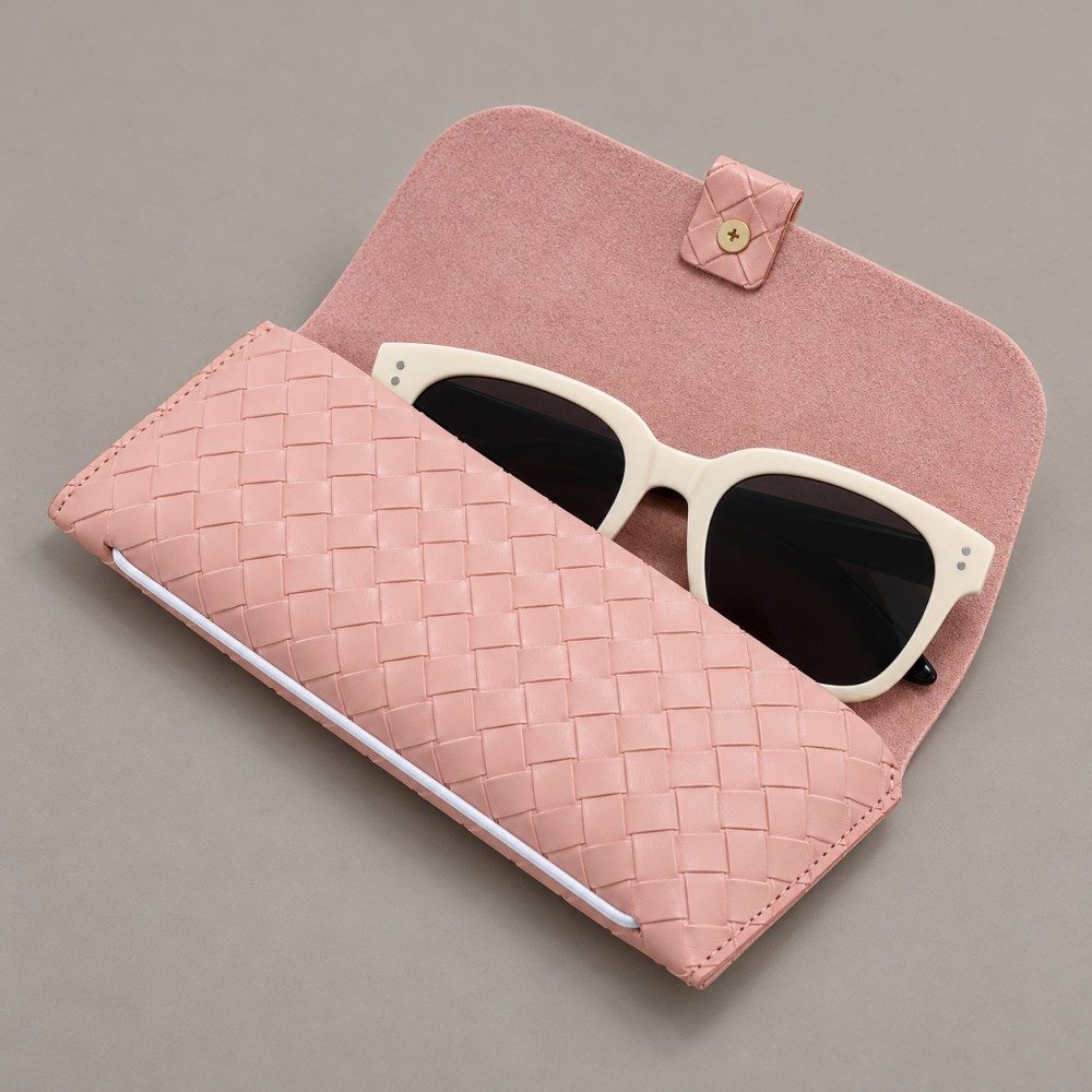 Open pink eyewear case holding cream-colored sunglasses and showing its soft pink lining and fastening tab.