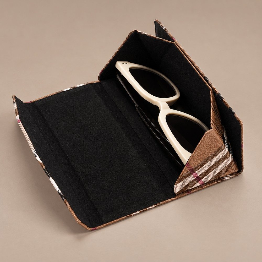 Open brown plaid folding glasses case showing black lining, folding side panels and cream-framed sunglasses inside.