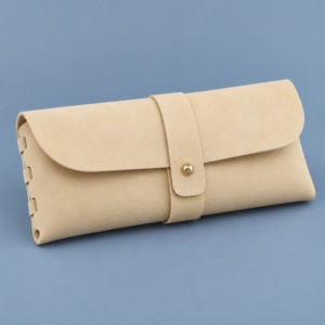 Pale yellow soft eyeglass case with a rounded flap, central wrap strap, gold-tone stud and laced side edge.