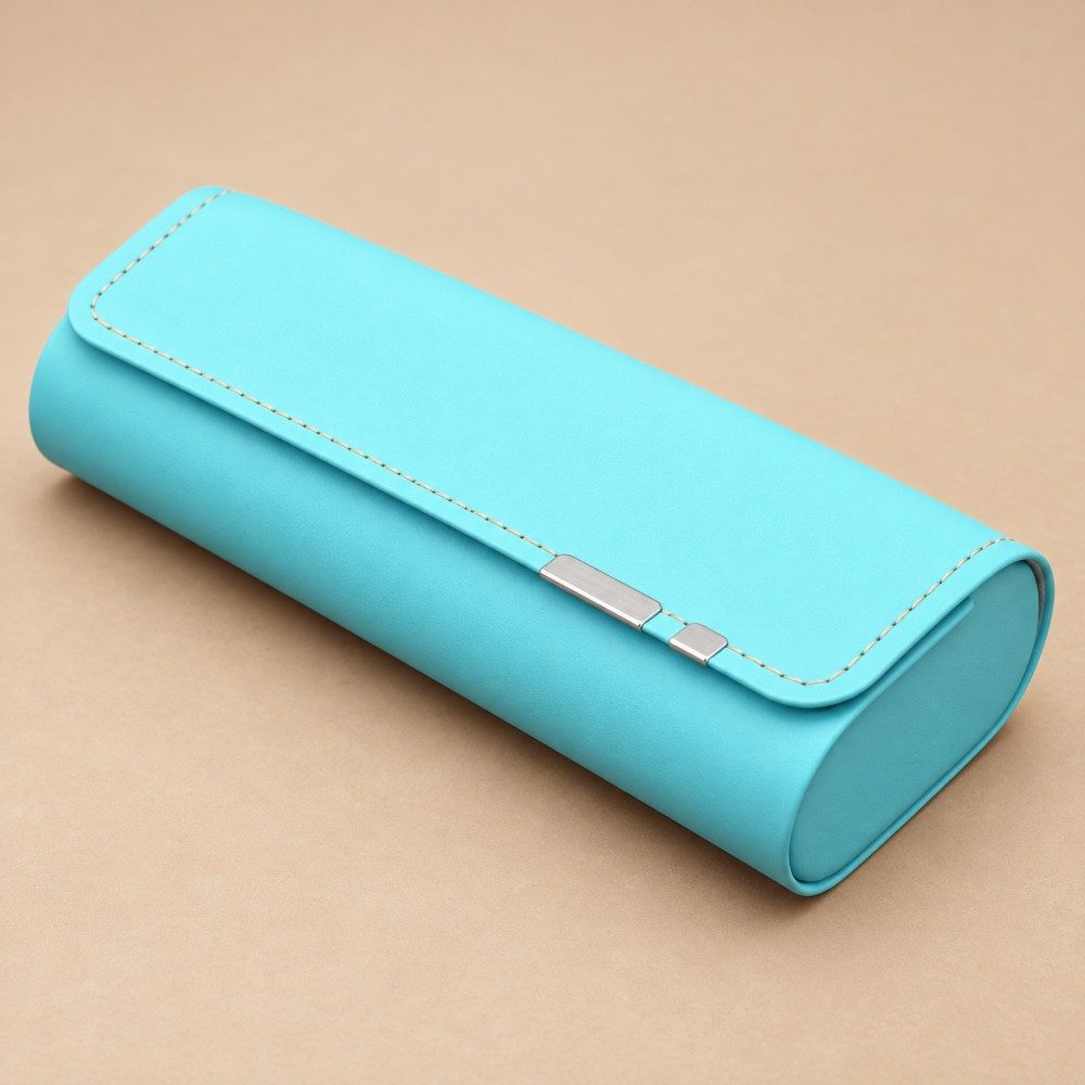 Turquoise magnetic closure glasses case with contrast stitching, rounded ends and two silver-tone flap accents on a sand background.