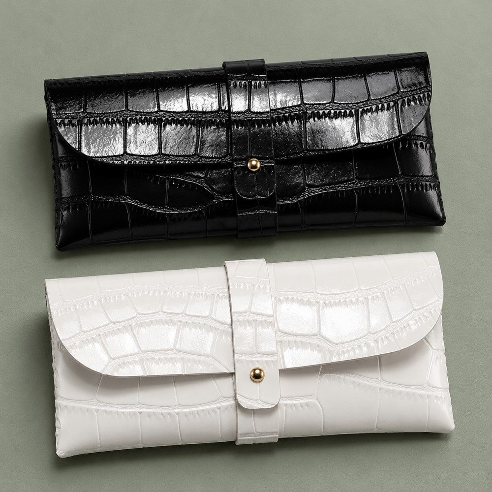 Black and white croc-embossed soft sunglasses cases with matching strap closures on a muted sage background.