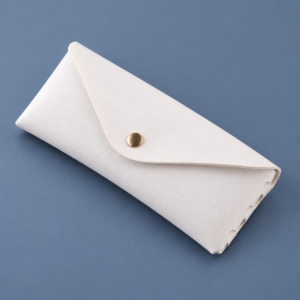White PVC synthetic leather glasses case with an envelope flap, gold-tone snap and hand-laced side edge.