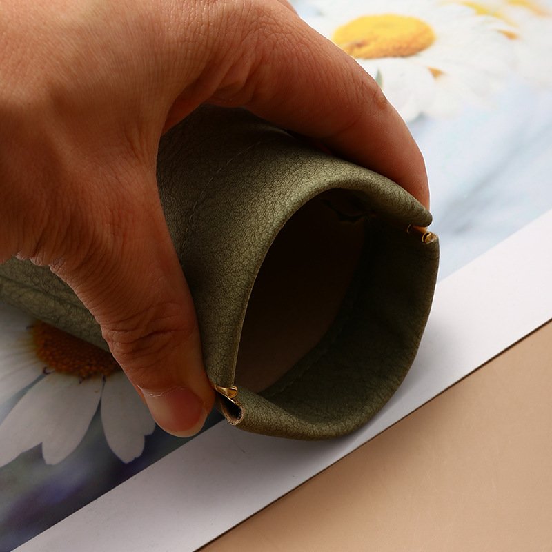 Close-up of a hand opening the spring frame on a green sunglasses pouch